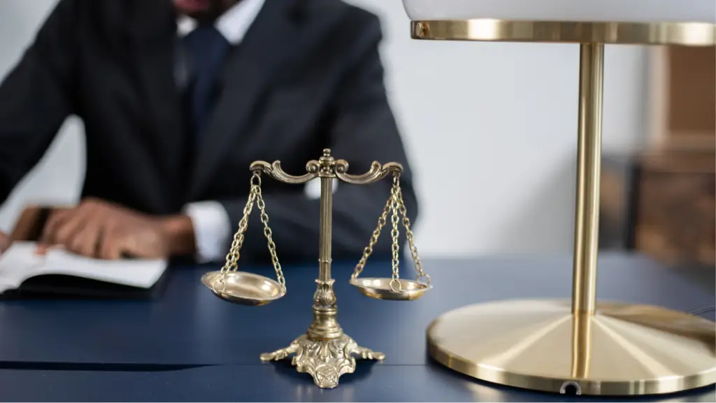 A set of balanced justice scales placed on a desk in front of a professional in a business suit, symbolizing fairness, accountability, legal judgment, ethical decision-making, and the balance between quality control and profitability.