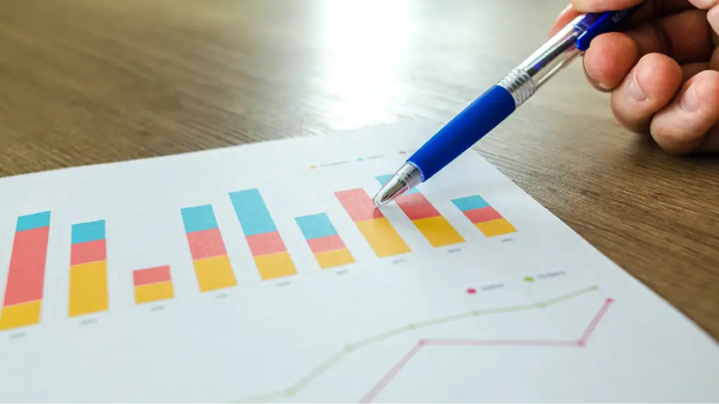 Optimizing Technical Frameworks for Local Intent A hand pointing a blue pen at a stacked bar chart on a printed document resting on a wooden desk.