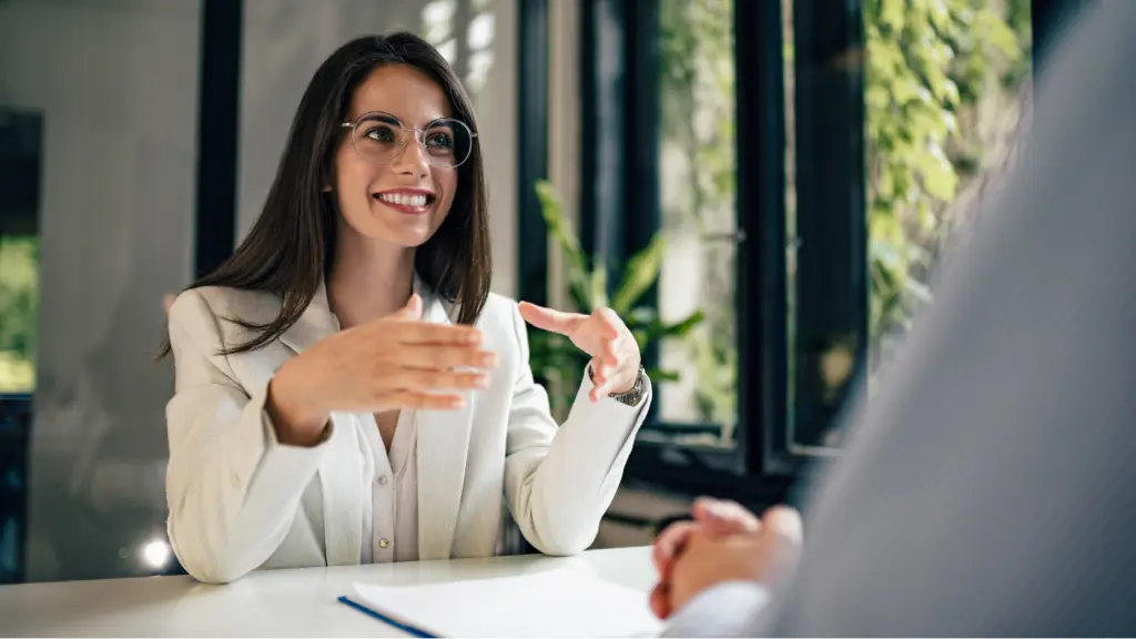 Securing Long-Term Client Loyalty (1) A smiling business professional engaged in a client meeting, gesturing during a conversation, representing trust, relationship building, long-term client loyalty, and effective business communication.