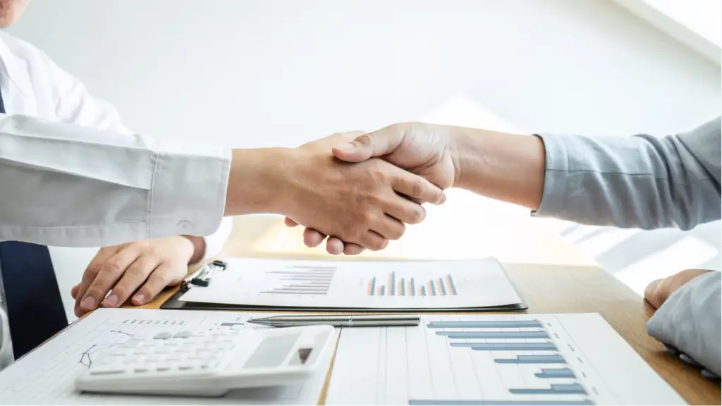 Securing Long-Term Client Loyalty (1) A business professional shaking hands with a client across a desk with financial charts and a calculator, symbolizing trust, long-term client loyalty, successful partnerships, and strong business relationships.