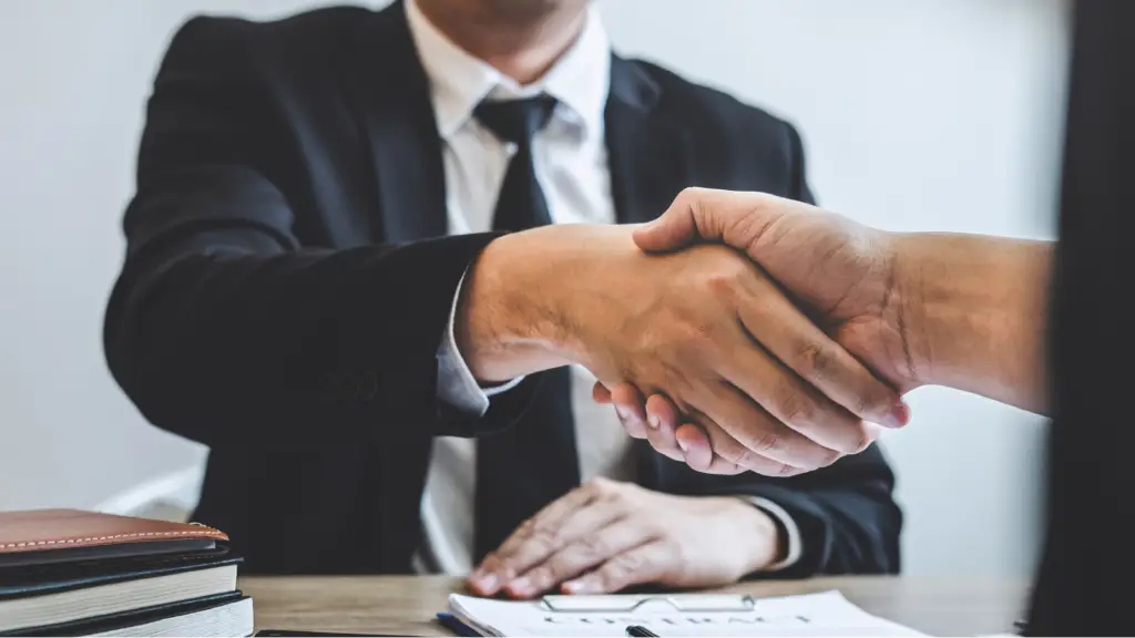 A business professional shaking hands with another person across a desk, symbolizing trust, partnership, long-term client relationships, and successful business collaboration.