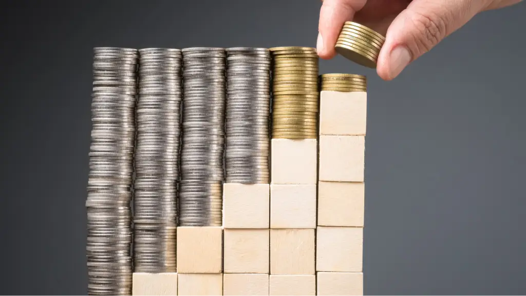 Securing Long-Term Performance and Market Longevity A hand placing coins on stacked columns of coins and wooden blocks, symbolizing long-term financial growth, performance optimization, investment planning, business sustainability, and market longevity.