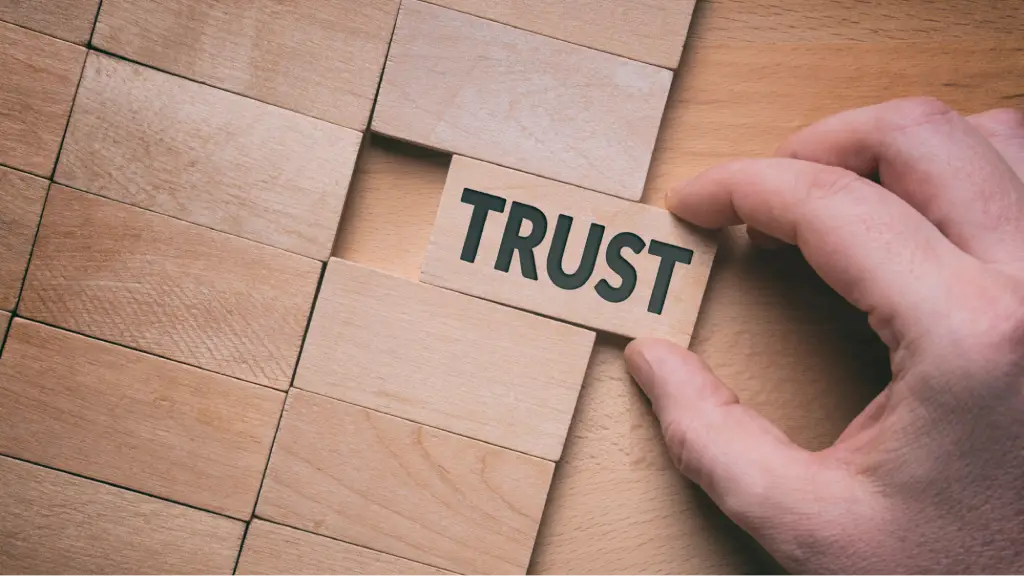 Strengthen Entity Recognition (1) A hand places a wooden block labeled “TRUST” into a puzzle, representing trust, credibility, and stronger entity recognition for improved online authority.